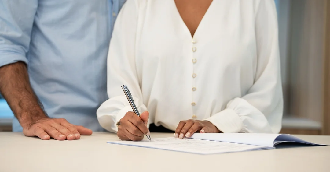 Young couple signing an apartment lease agreement with a property manager at a desk in a rental office.